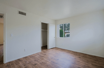 A room with a wooden floor and a window with window coverings showing trees outside at Sahuaro West Phoenix, AZ